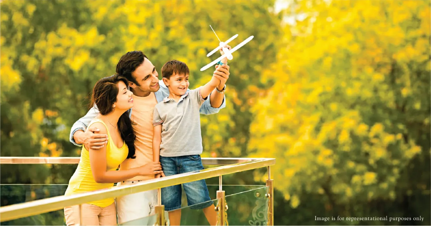 Family on a wide sundeck with a glass balustrade and tree canopy beyond, representative of the sundecks at Rustomjee Urban Woods